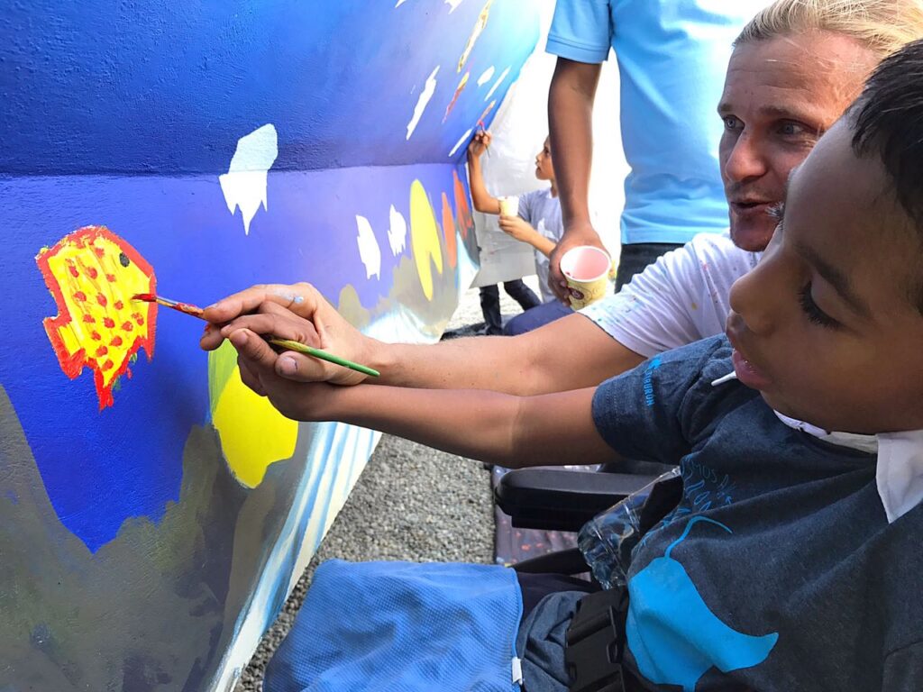 Carlos Hiller artist painting a public mural with kids help.